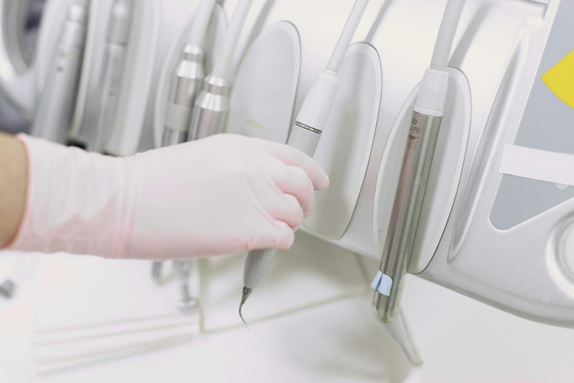 Primer plano de una mano enguantada manipulando instrumentos dentales en un entorno clínico estéril.